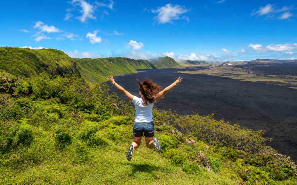 Woman jumping with arms raised over a volcanic landscape in the Galápagos
