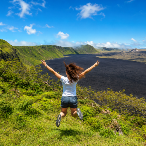 Woman jumping with arms raised over a volcanic landscape in the Galápagos