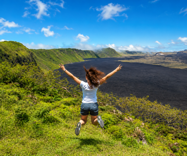 Woman jumping with arms raised over a volcanic landscape in the Galápagos