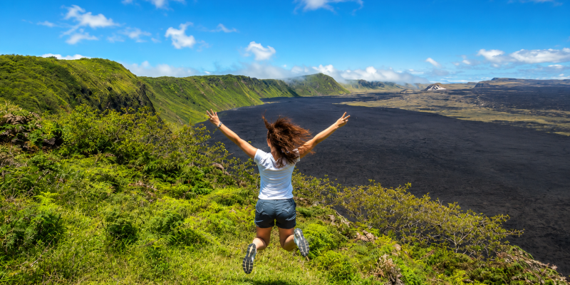 Woman jumping with arms raised over a volcanic landscape in the Galápagos