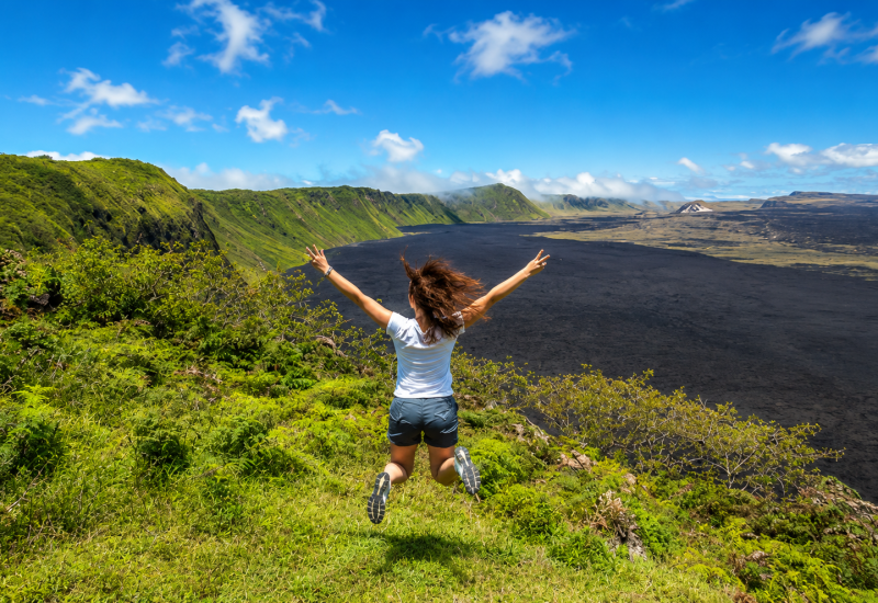 Woman jumping with arms raised over a volcanic landscape in the Galápagos