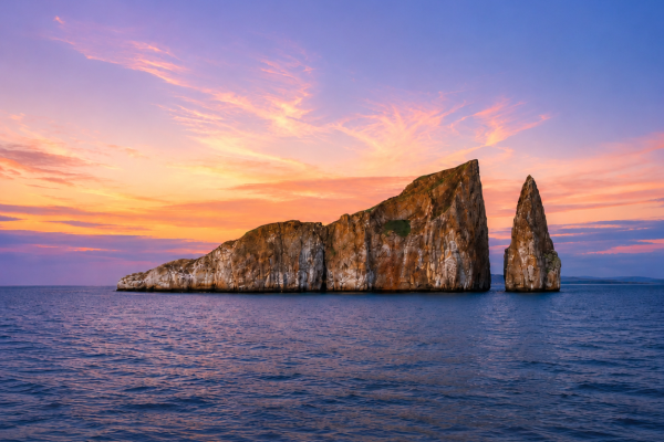 Galápagos rock formation rising from the ocean beneath a colorful sunset sky